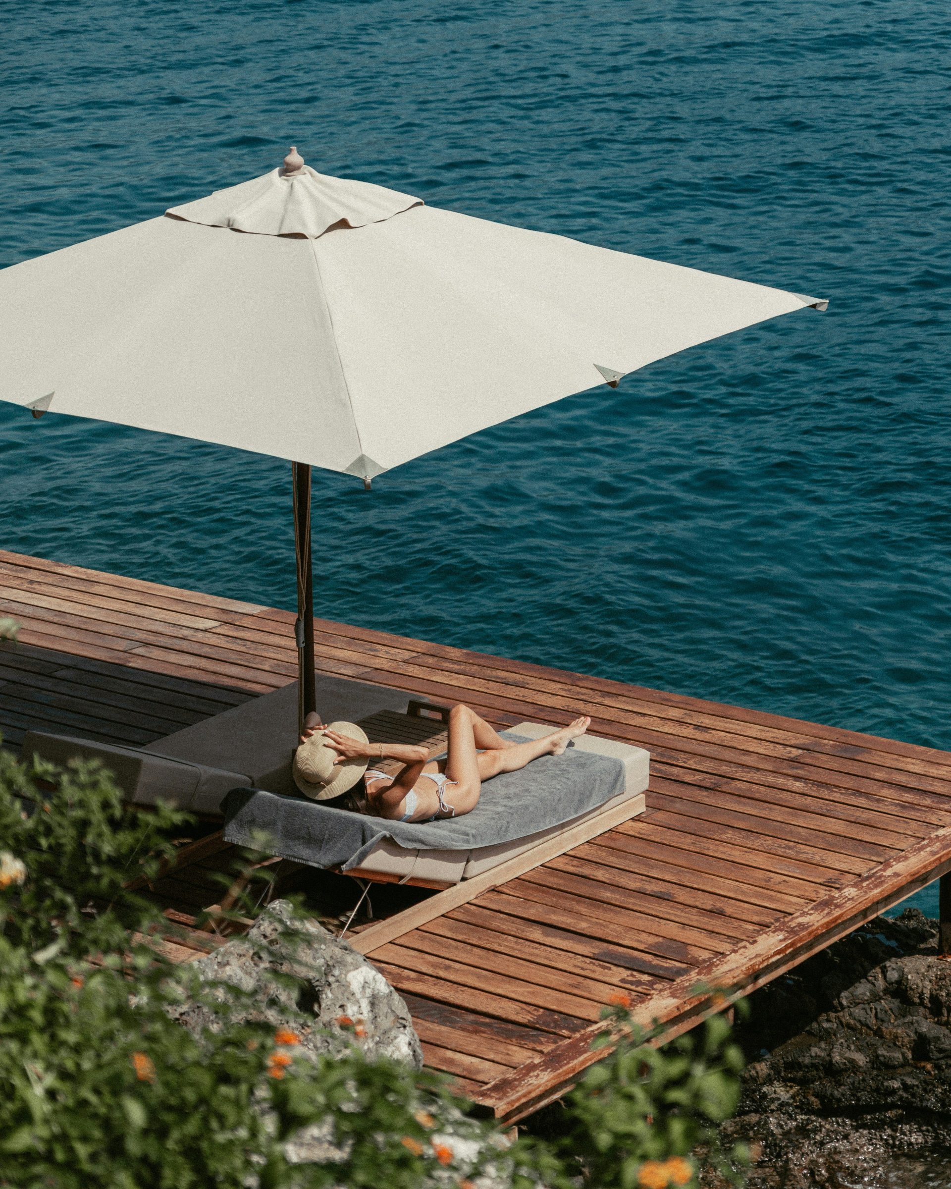 Woman sunbathing on a dock near the ocean.